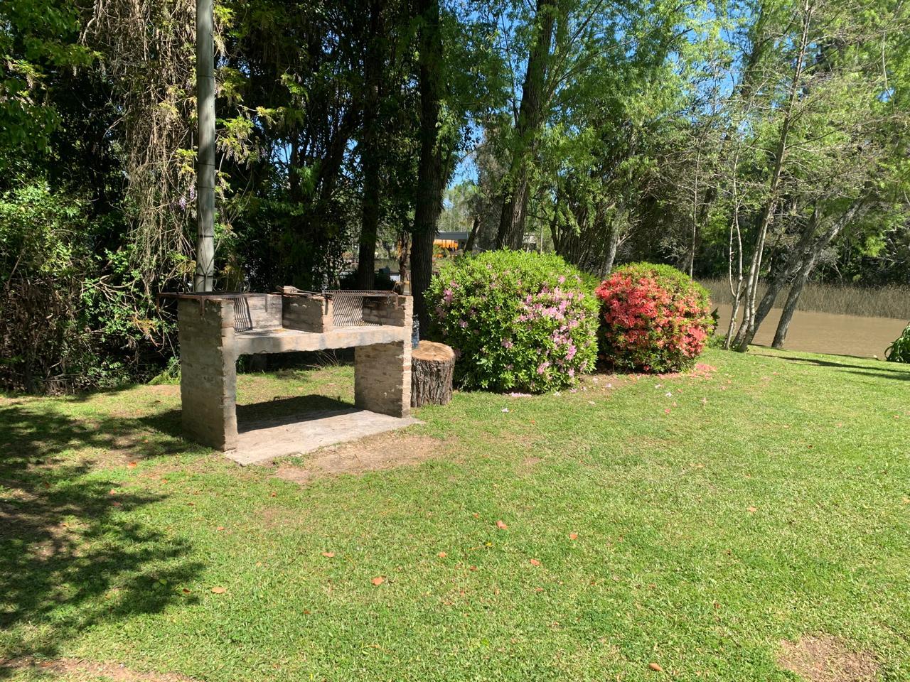Parrilla exterior entre flores, con el arroyo de fondo